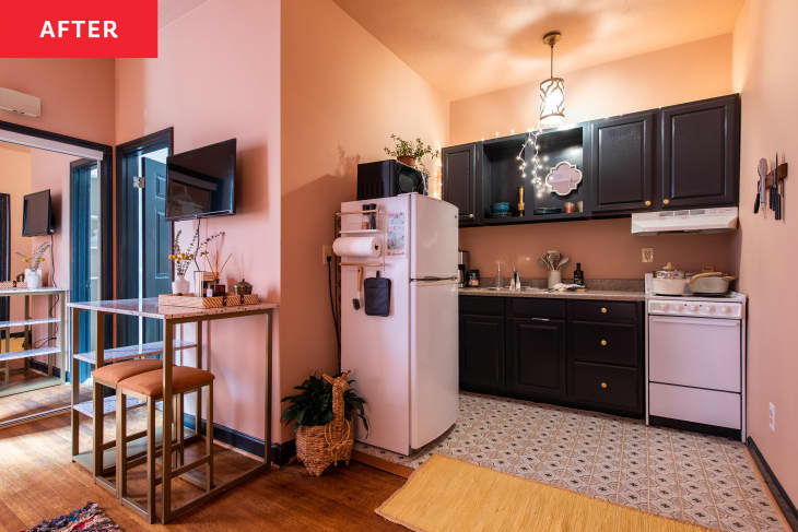 Kitchen after makeover. Pink walls, black cabinets, pendant light. To the left is a dining counter with stools