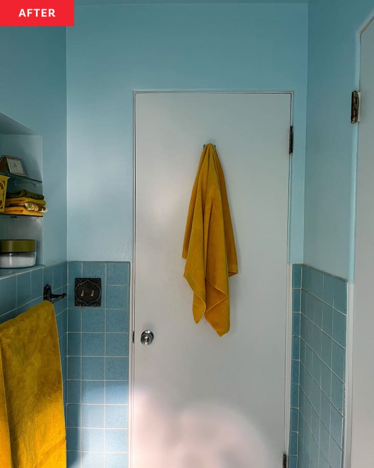 Blue bathroom with mustard colored towel hanging on back of door.