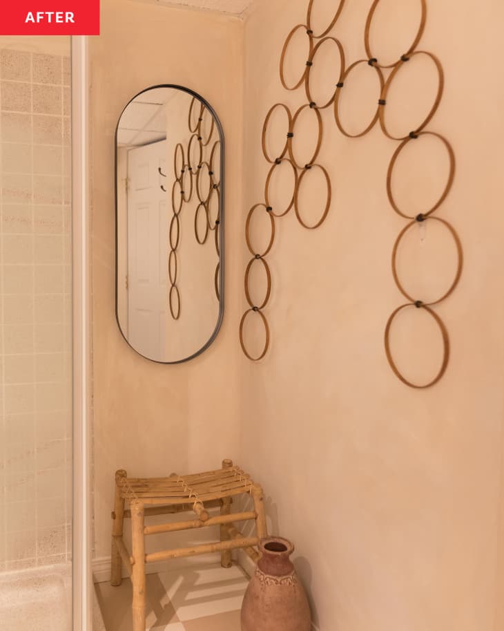 Oblong mirror and wall art in newly renovated bathroom with wooden stool and terra cotta vase.