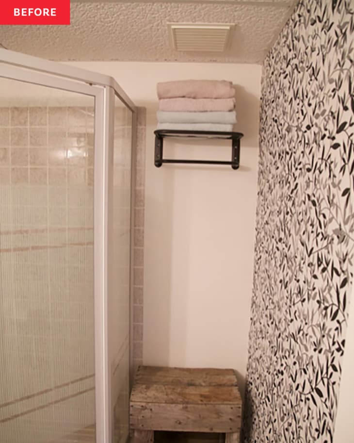 Towels folded on floating shelf in bathroom with black and white leaf print wallpaper before renovation.