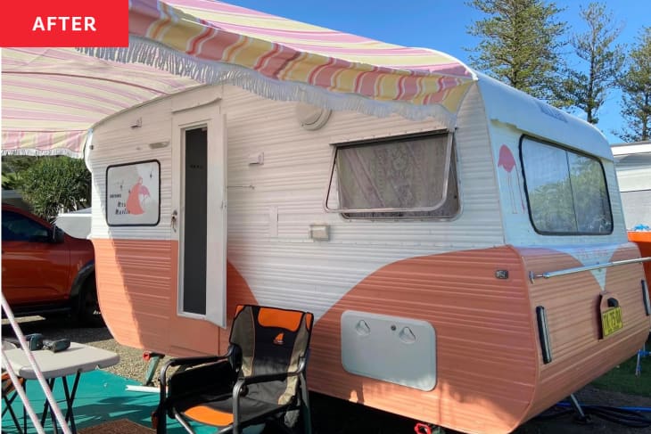 Exterior of caravan/camper after renovation: coral and white paint, pink flamingo, text that says "Driving Mrs Marlie". Yellow and pink and white fabric overhang with white fringe trim, table and chairs set up outside