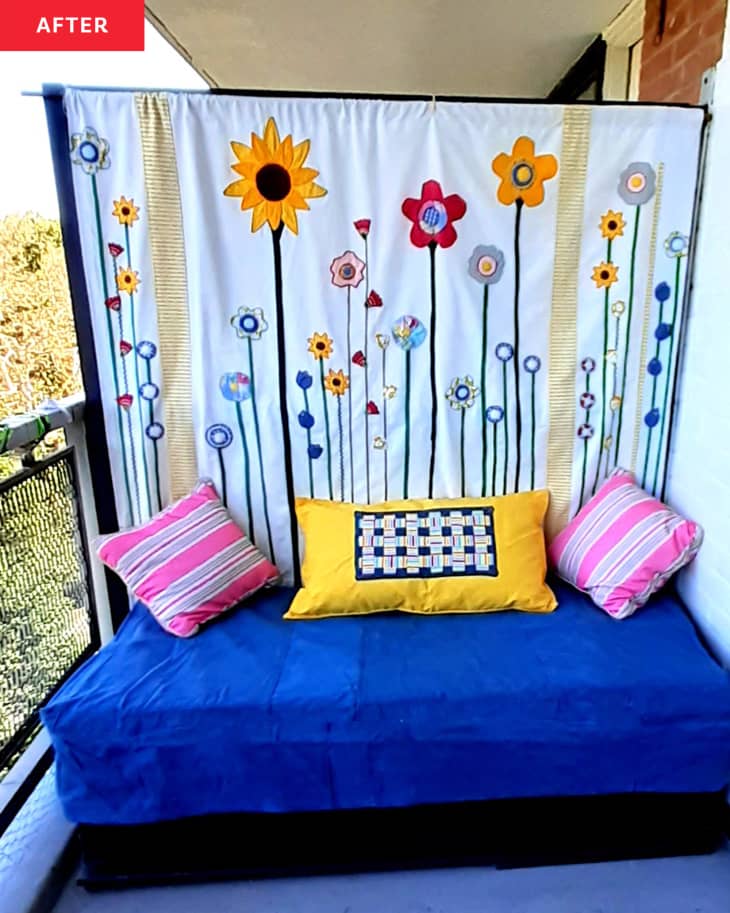 Balcony after makeover/renovation with blue small sofa/daybed with pink and yellow pillows in front of partition covered with handmade wall hanging of flowers made from fabric scraps