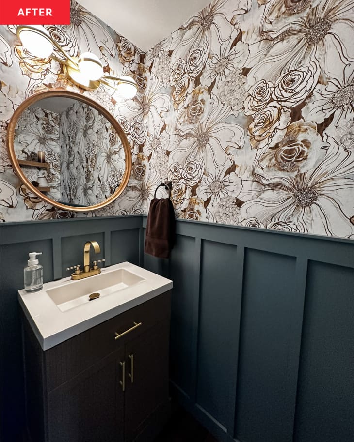 bathroom after makeover: gold framed round mirror over sink, floral illustrated wallpaper, gold hardware, deep blue walls