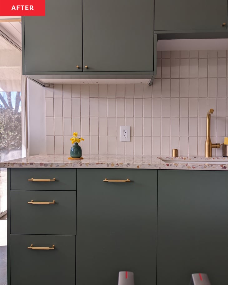 Kitchen after renovation: green cabinets with brass hardware, white tile backsplash, terazzo countertops