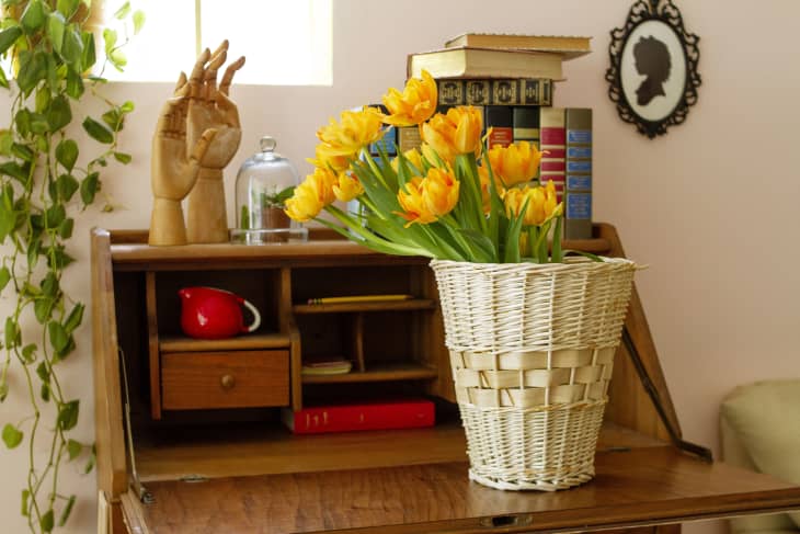 Bleached wicker basket holding flowers, resting on a wood secretary desk