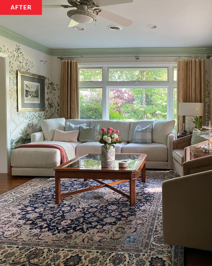 Living/family room with pale green tree and bird wallpaper, green and white trim, large window behind pale gray sofa, large wood and glass coffee table with vase of flowers