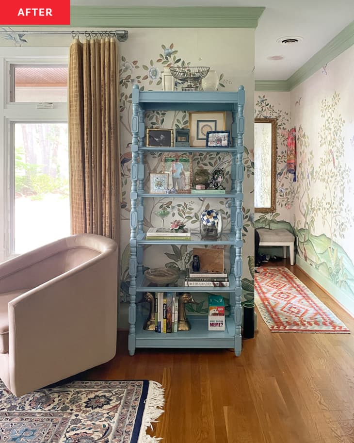 Living/family room with pale green tree and bird wallpaper, green and white trim, light blue tall shelves with books, framed photos, pale blush armchair