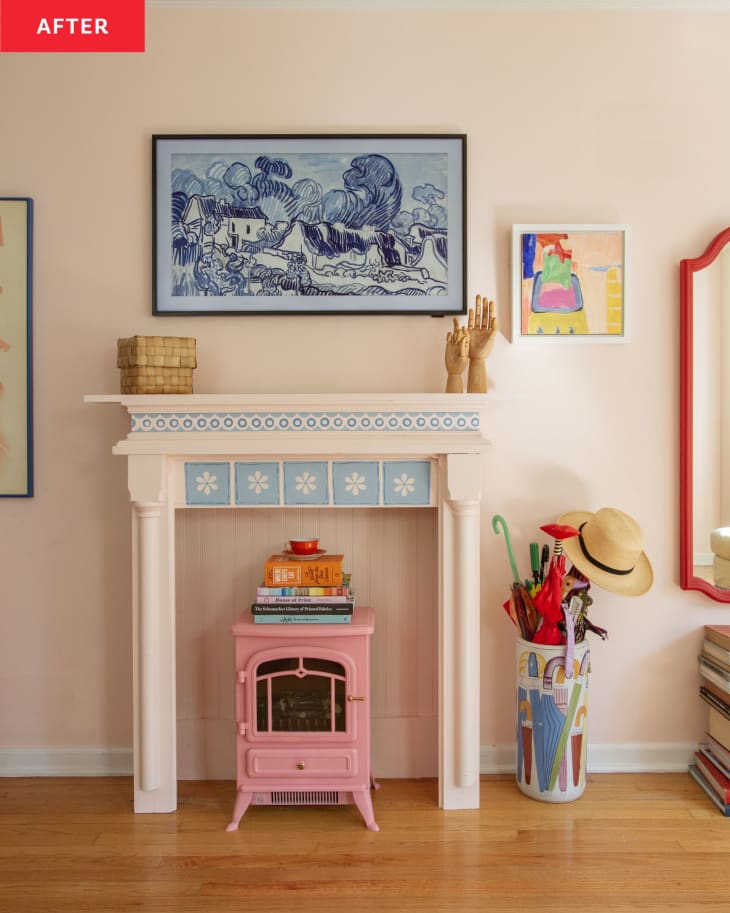 After: A pink fireplace surround with a pink electric fireplace in the hearth, set against a pink living room wall. There is art on either side of the faux fireplace, and a Frame TV hung above it with a blue and white landscape on display.
