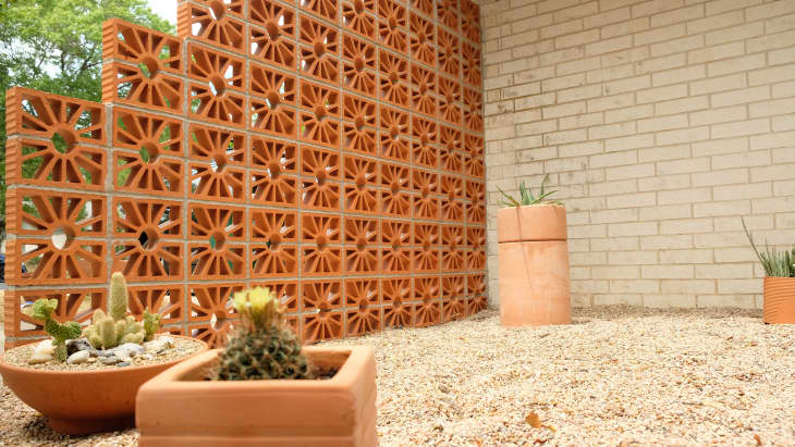 Front exterior (curb appeal) of home after makeover: terracotta breeze blocks with sand-colored gravel, succulents in terracotta planters, cane chairs with sherpa throws, sand-colored brick back wall