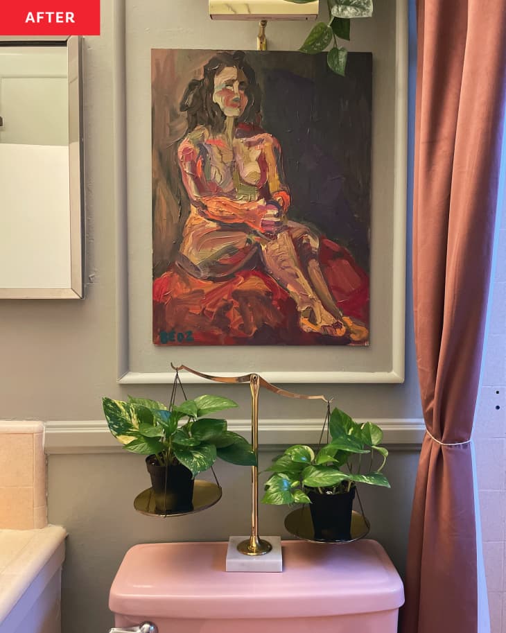 Painted portrait hung in bathroom above toilet. Two plants balanced on scale on top of pink toilet.