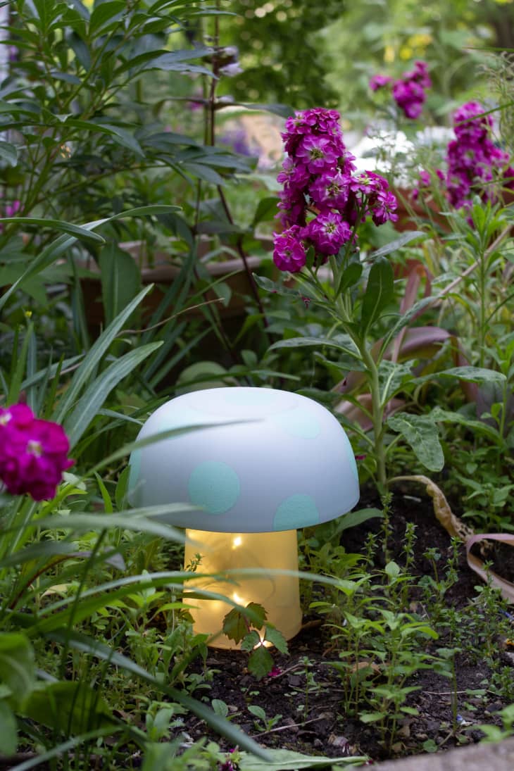 DIY mushroom lawn decor with fairy lights in the bottom, displayed in a garden.