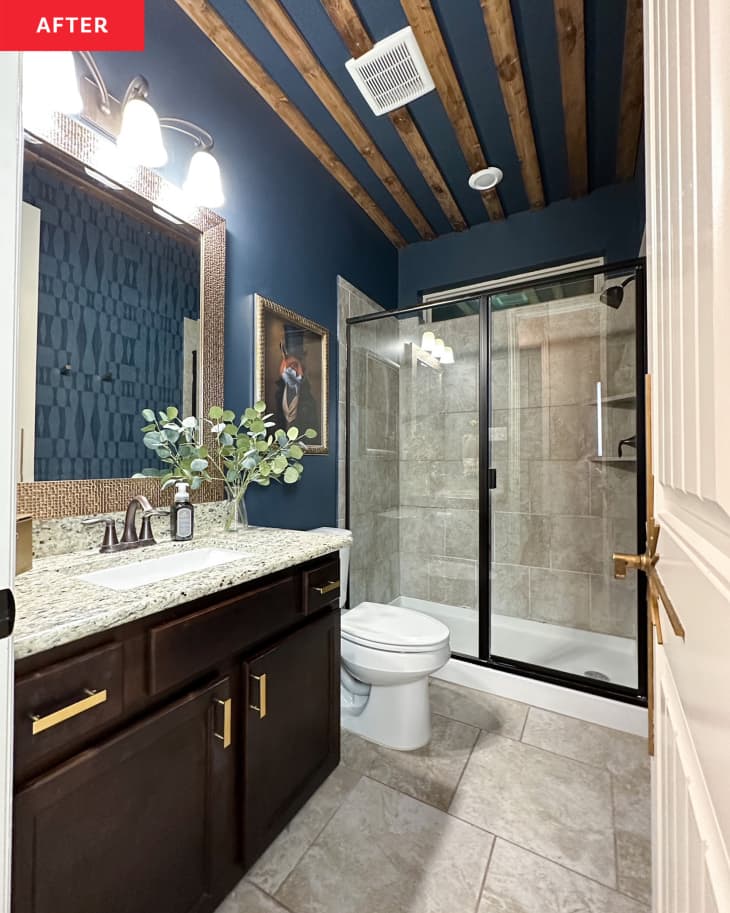 Navy painted bathroom with wooden beams on the ceiling and newly framed mirror in bathroom after renovation.