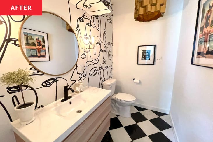 不wly renovated bathroom with black and white checkered tile and black and white face doodle wallpaper. Round mirror above bathroom vanity with two sconces on either side.