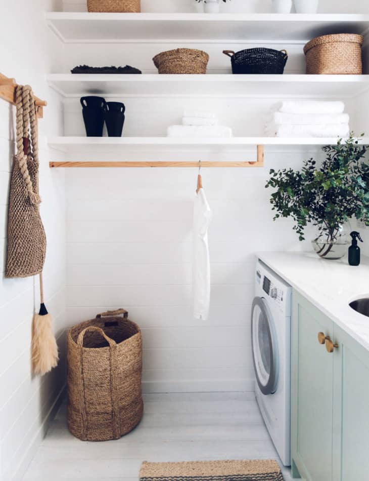 a wooden hanging rail, with a white shirt on a hanger, attached to the bottom of a white laundry room shelf