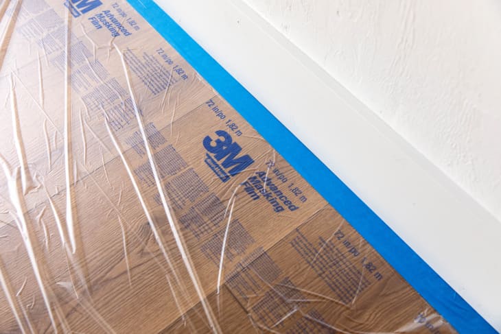 Painter's tape and film covering the floor next to baseboards prior to painting
