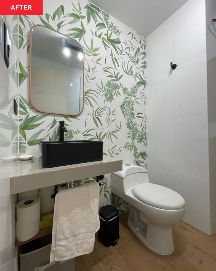 Green and white wallpaper in newly renovated bathroom with black sink and new mirror.