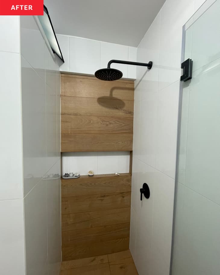 Newly renovated shower with wooden toiletry shelving and black hardware fixtures.