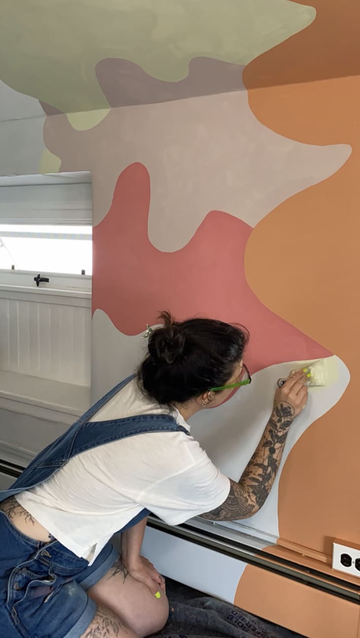 DIYer painting in a mural on her wall using a short-handled paint brush.