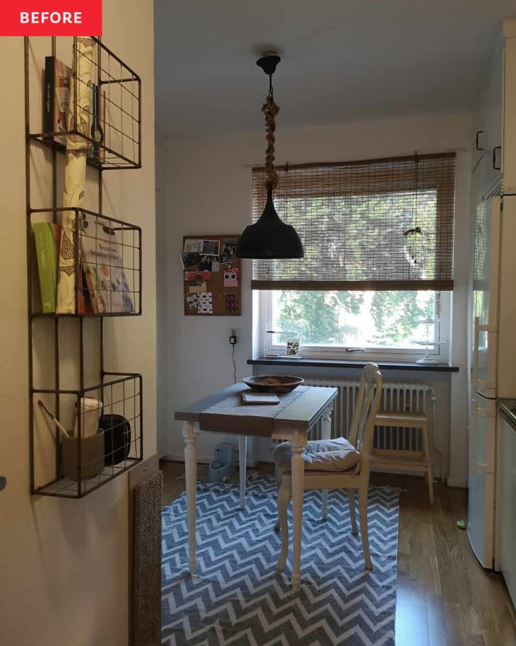 grey and white zig zag stripe rug, black hanging light fixture with chain cover, wood desk table with one wood chair, beige chair cushion, wood stool, white walls, white radiator, bamboo shade, cork board, wood floors, black spice rack