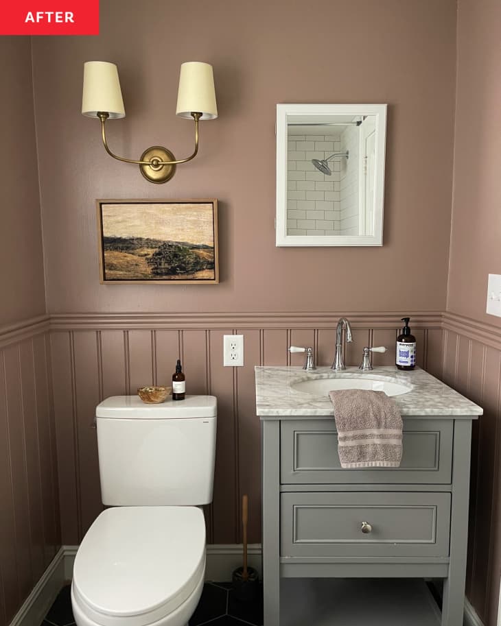 bathroom after remodel/makeover: brown walls, brass sconce, wainscoting, gray/green sink with marble counter, white tiled shower, dark gray tiled floor