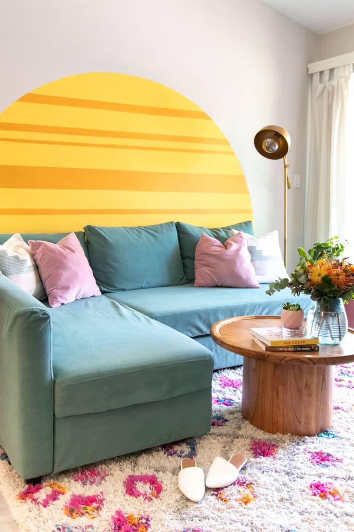 A yellow sunset design on a white wall behind a green couch