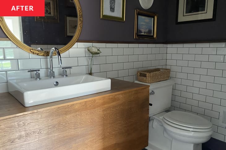 white subway tile, purple wall half up, large wood vanity, raised white sink cowl, round gold mirror, white toilet, woven basket, gallery art wall