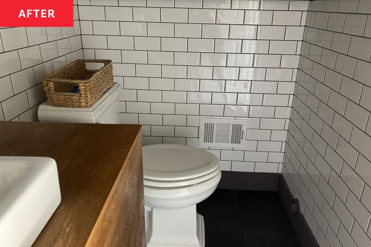 white subway tile, dark floor, wood vanity, white sink bowl raised, woven basket on toilet