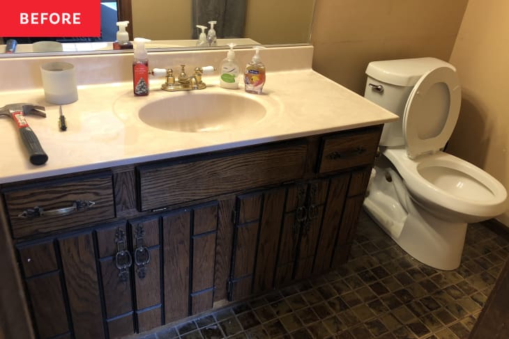small square brown tile floor, old wood panel vanity, white counter top, white toilet, grey towel, beige walls, mirror, hammer