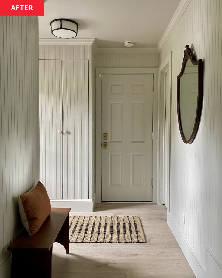 white tongue and groove paneling, wood floors, beige and black runner, dark wood bench, orange throw pillow, molding, vintage mirror with rounded bottom, white door, closets