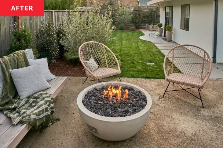 Fire pit in newly renovated backyard with two wicker chairs on other side of fire pit.