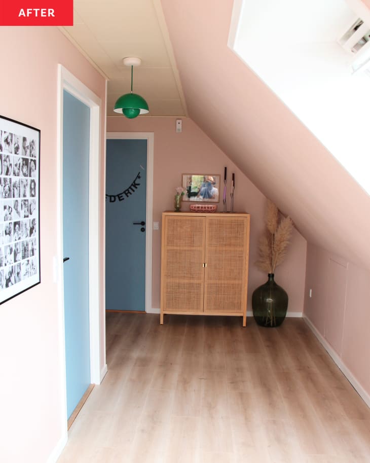 pink walls, wood floors, rattan two door cabinet wardrobe, blue doors, banner on one door, green half orb lighting fixture, family picture collage, floor vase with dried leaves, white door trim, sky light, angled ceiling