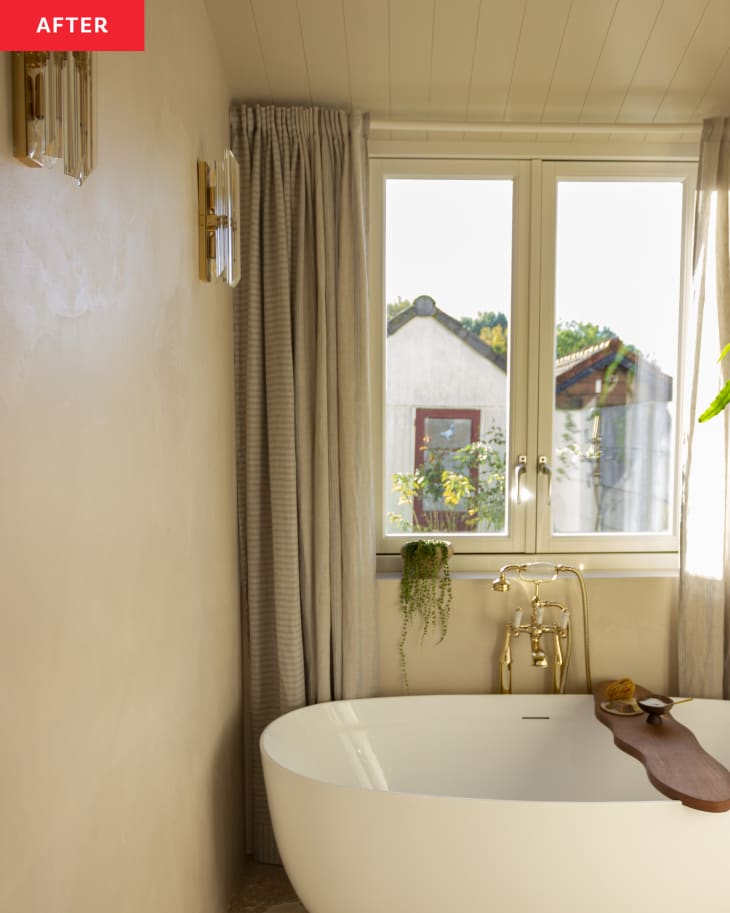 A large window above a white tub in a beige room.