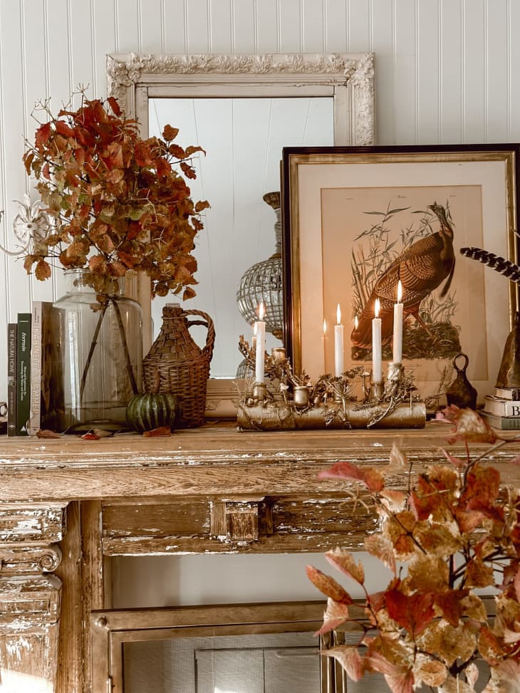 Mantel decorated with rustic decor, including branches, wicker bottle holder, and a gilded mushroom candelabra.