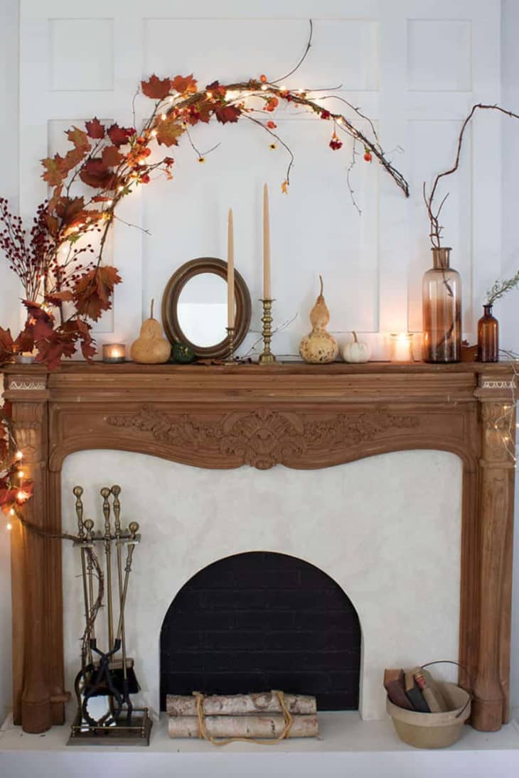 Wood fireplace mantel with an arch above created with branches, faux leaves, and string lights.