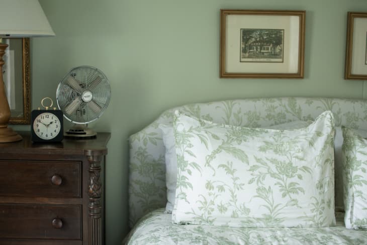 Bedroom with soft green walls and a green-and-white floral print headboard with matching duvet cover.