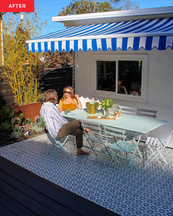 white house with black and white tiled large deck in yard: dining table and chairs with 2 people sitting