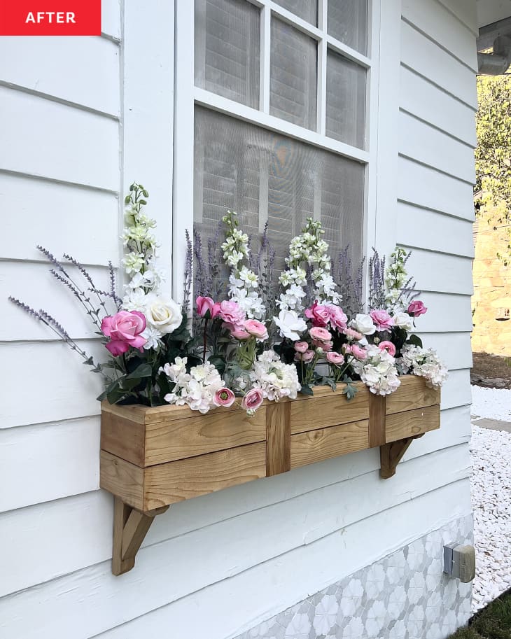 A wooden flower box on the side of a white house