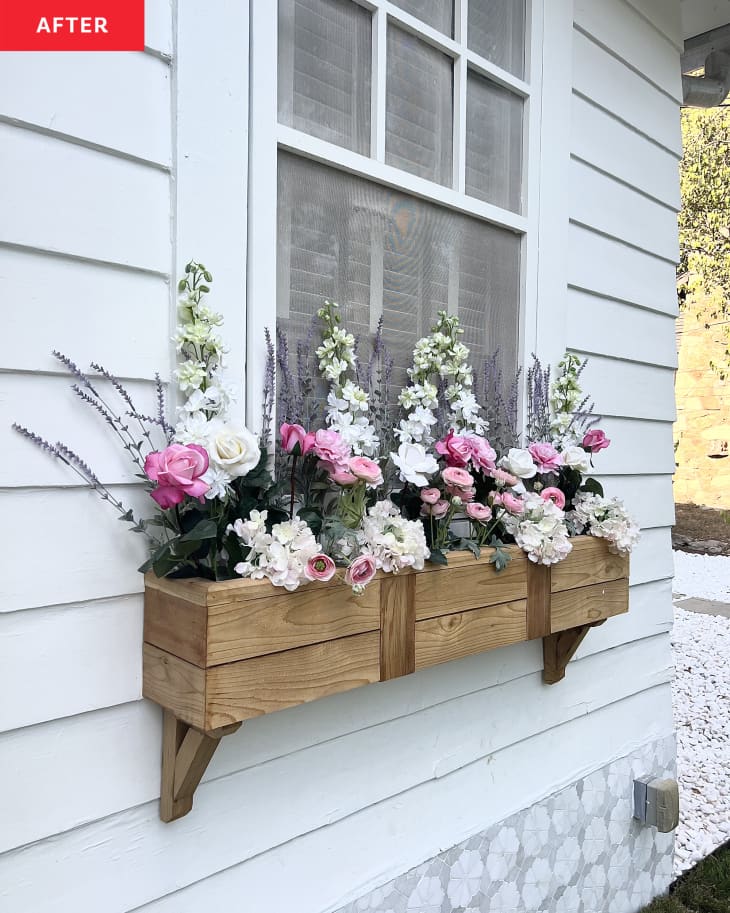 A wooden flower box on the side of a white house