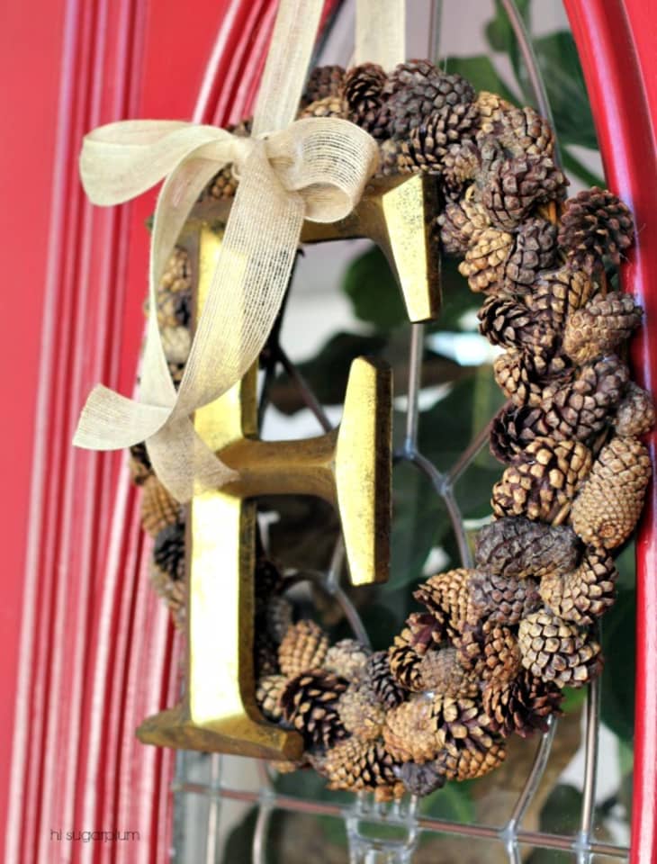Pinecone wreath with large decorative gold "F" tied with ribbon to the front.