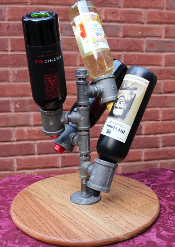 Tabletop wine storage made from metal pipes, holding four bottles by the necks with corks facing downward