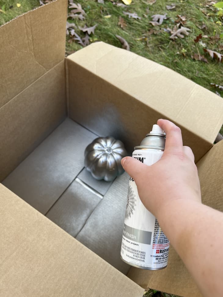 Spray painting a faux pumpkin with silver spray paint
