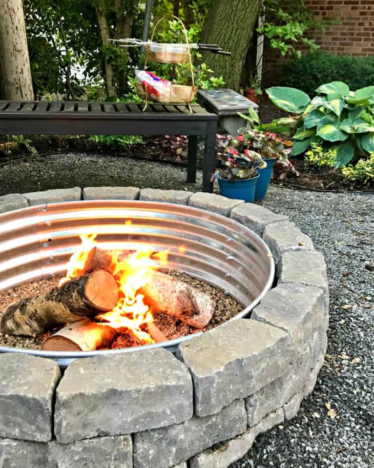 DIY fire pit made using stones surrounding a metal ring with logs inside.