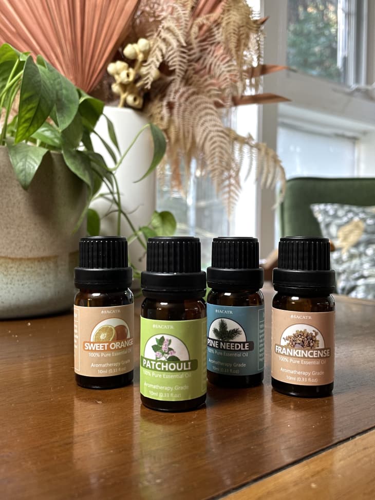 Bottles of essential oils on a table, including sweet orange, patchouli, pine needle, and frankincense.