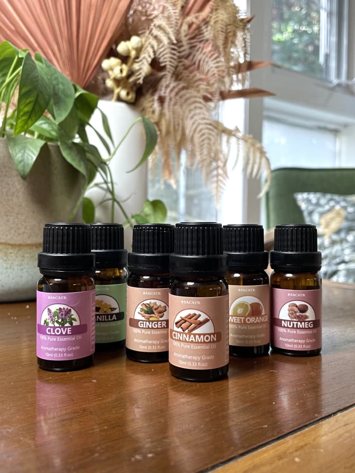 Bottles of essential oils on a table, including clove, vanilla, ginger, cinnamon, sweet orange, and nutmeg.