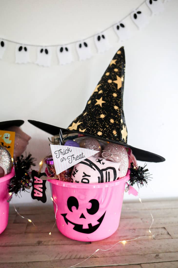 Plastic bucket with a Jack-o-lantern face on its front, filled with Halloween treats and topped with a black witch's hat.