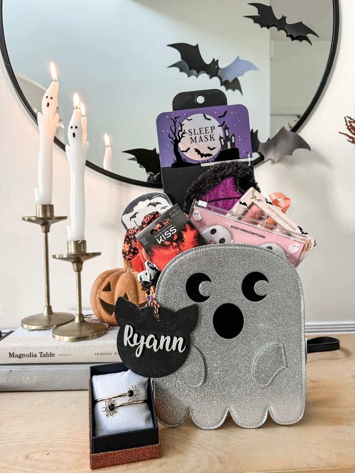 Silver-toned ghost basket with Halloween gifts inside, including a sleep mask, a spider bracelet, and more.