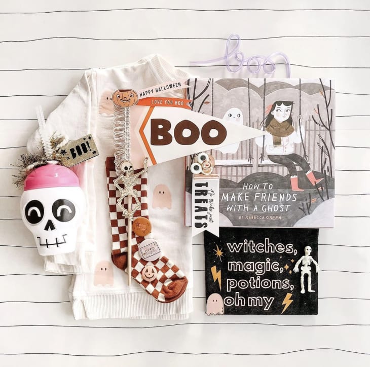 Hallween-themed gifts laid out on a table, including a ghost-patterned shirt, a skeleton straw cup, a book, a flag that reads "boo" and more.