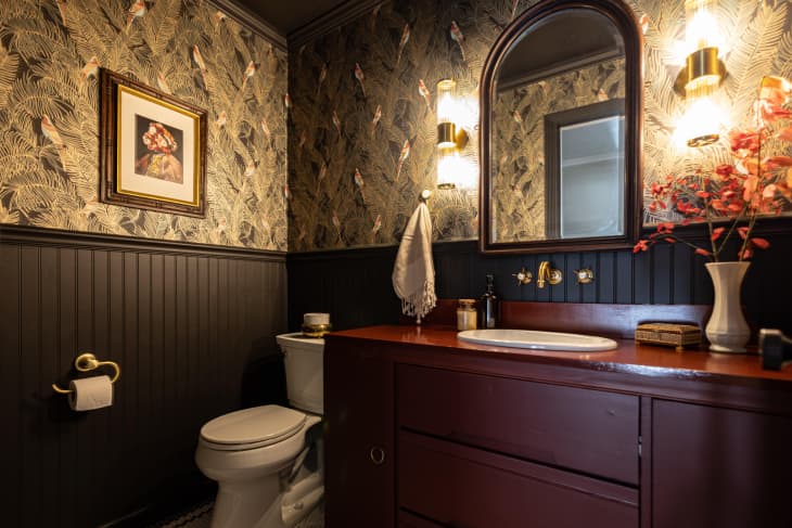 Black painted wainscoting in bathroom with feather motif wallpaper and maroon painted vanity.