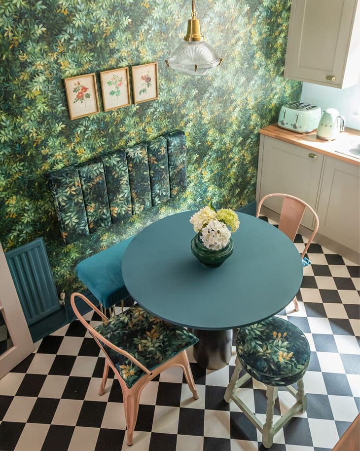 Kitchen with floral wallpaper with circular green table with pink chairs.