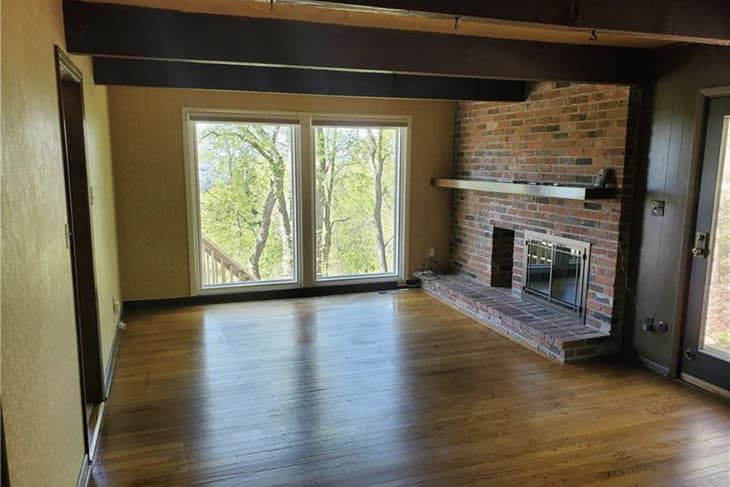 empty family room with yellow wallpaper, brick fireplace, and lots of wood before renovation